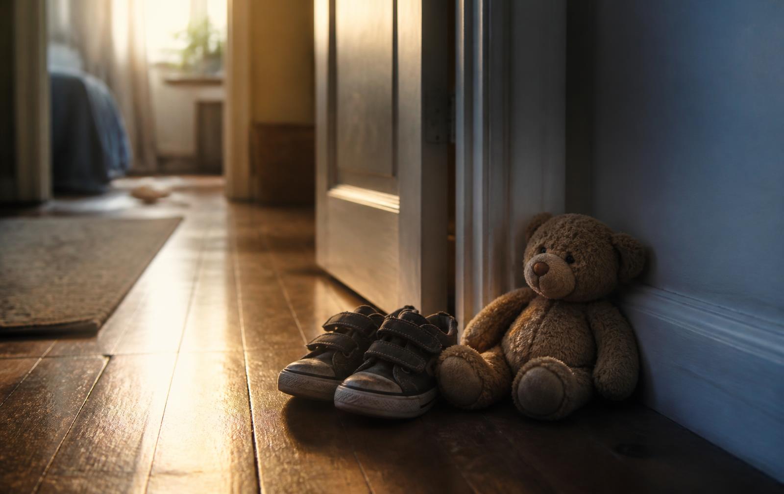 A child's small sneakers and a stuffed bear left in a sunlit hallway